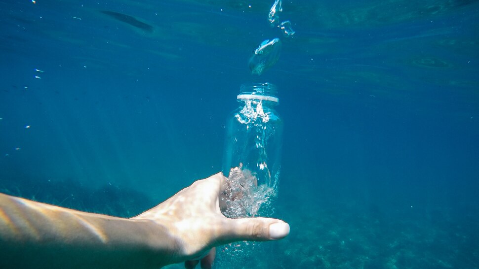 Hand hält Wasserflasche im Meer
