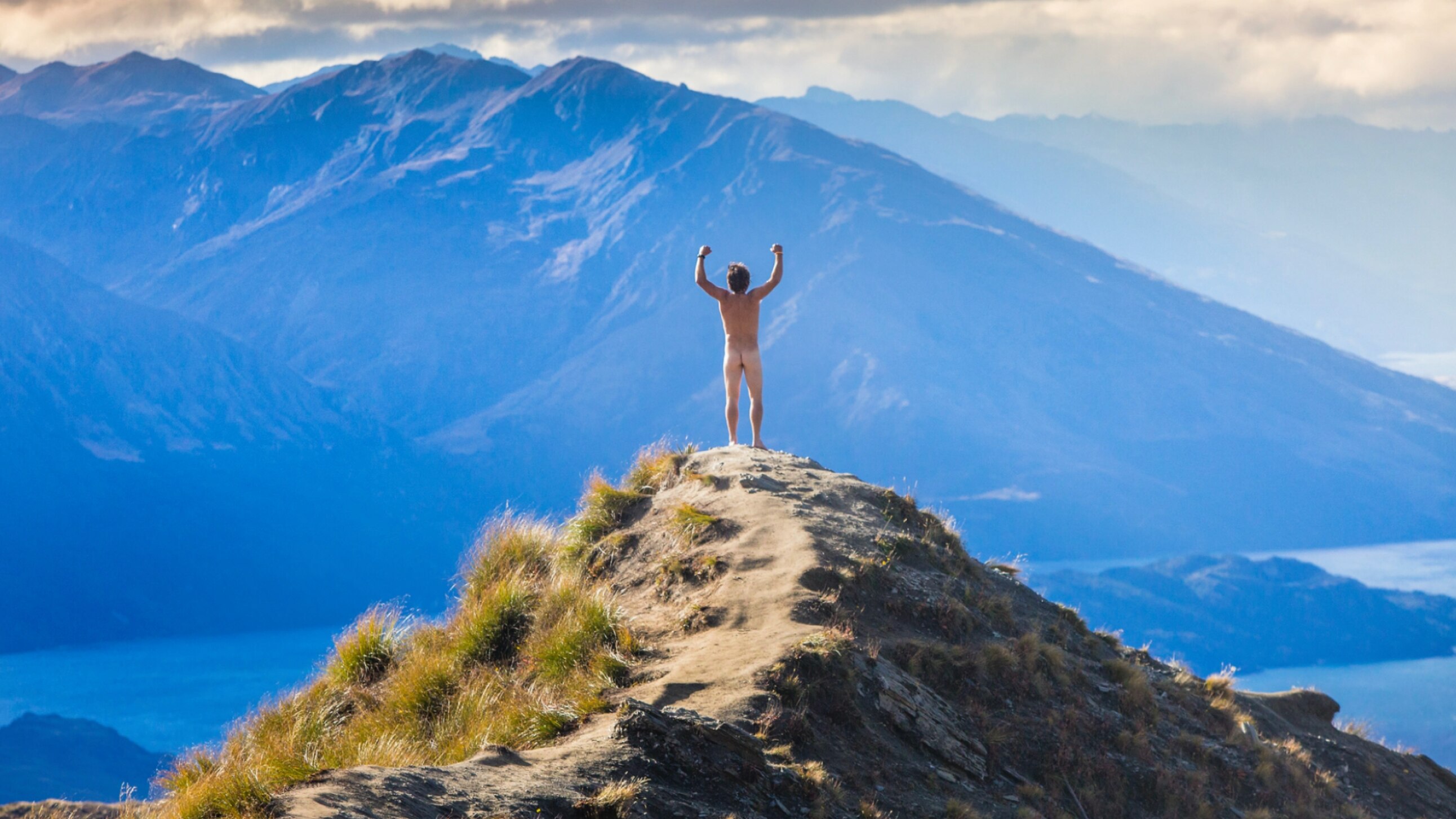 Homme nu debout sur une montagne, les bras en l'air