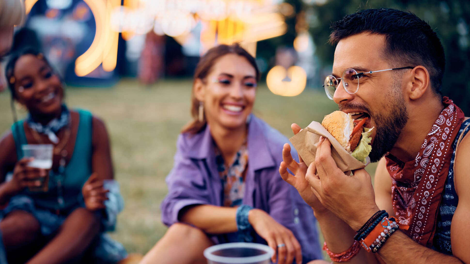 Freunde sitzen auf einem Festival zusammen und essen Burger