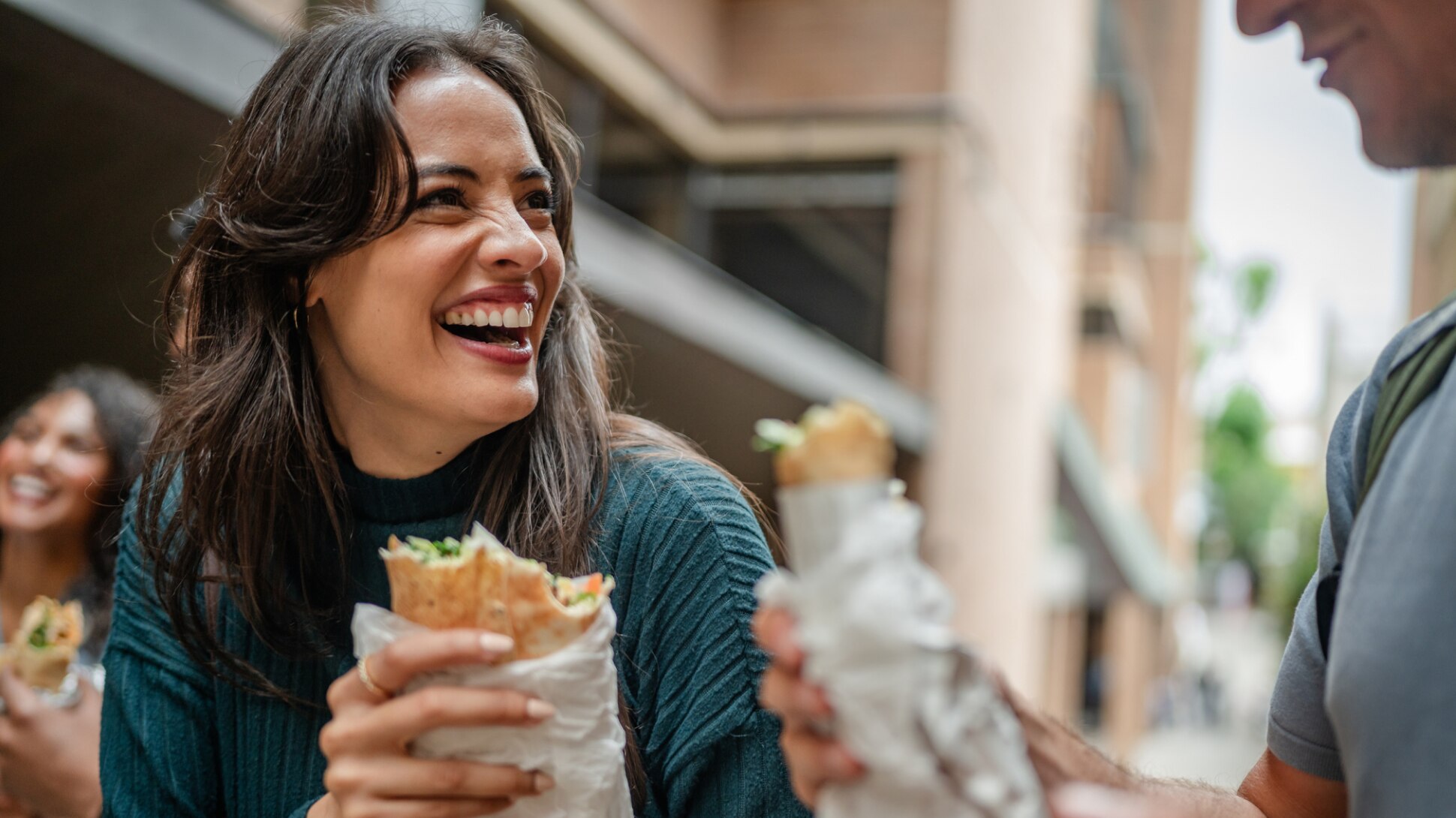 Junge lachende Frau isst ein gekauftes Sandwich