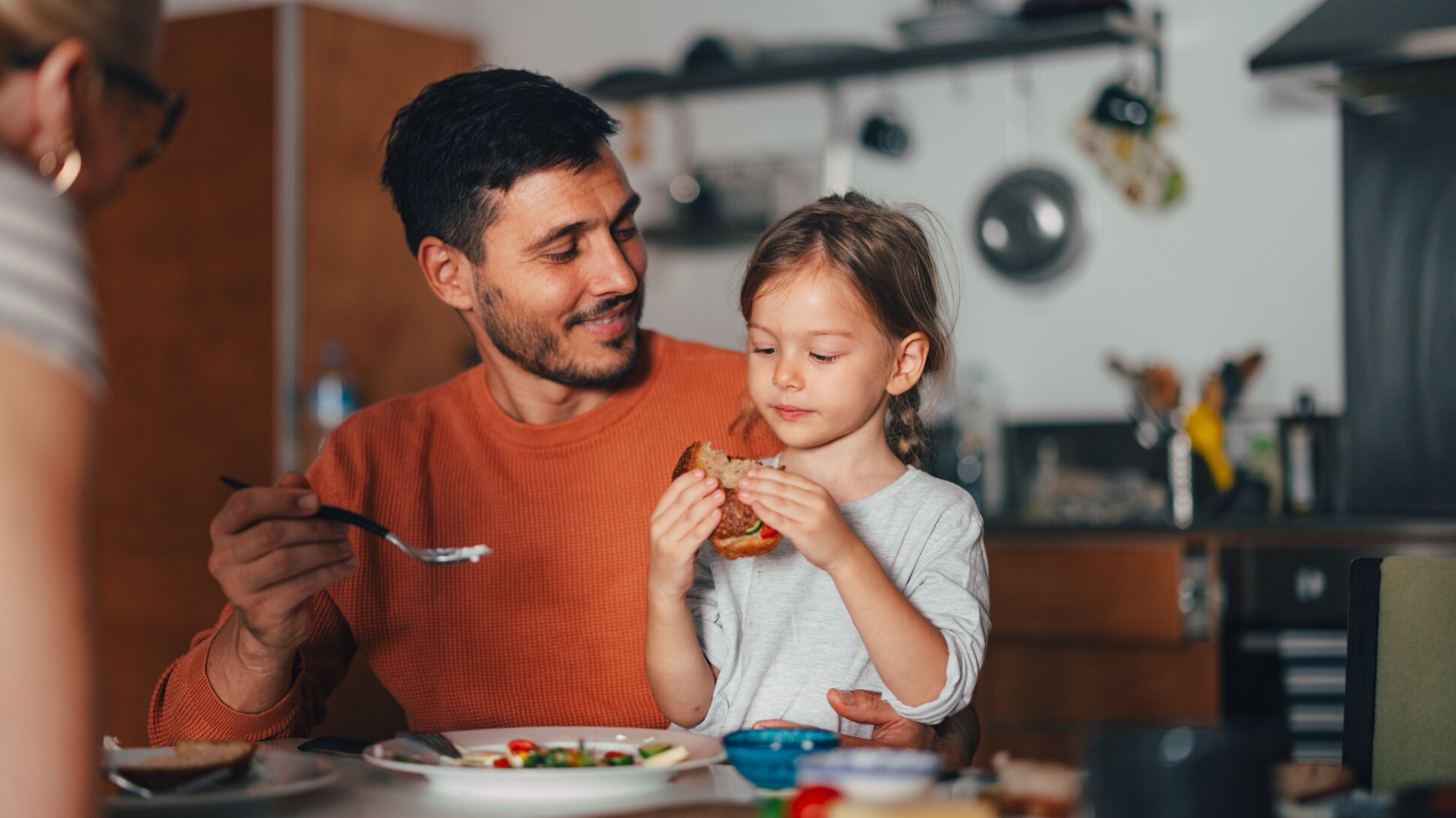 Ein Mädchen isst mit seinen Eltern ein Sandwich