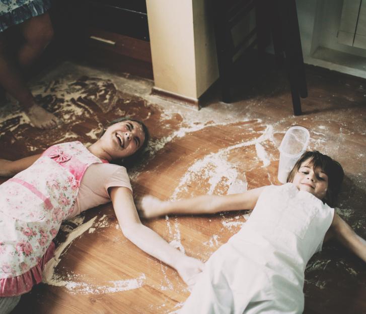 Zwei Kinder spielen lachend im Mehl auf dem Boden