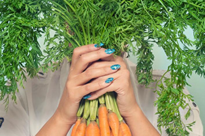 Frau hält einen Haufen gesunder Möhren vor ihrem Gesicht