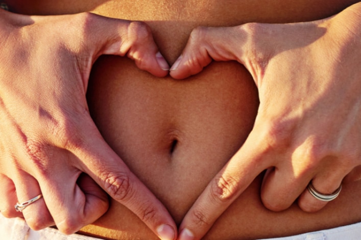 Frau hält ein Herz auf ihren Bauch 