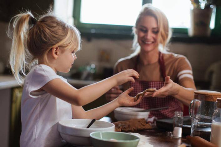 Maman et fille préparent des douceurs dans une cuisine ensoleillée.