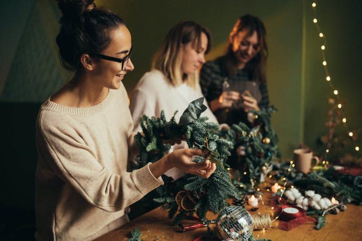 Femmes heureuses fabriquant une couronne de Noël avec des branches de pin et des décorations festives.