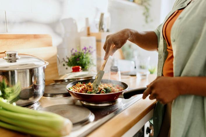 Femme préparant un mélange de légumes et de quinoa dans une poêle
