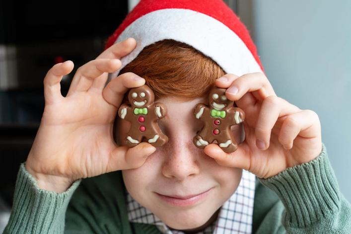 Portrait d’un jeune garçon cachant ses yeux avec des bonhommes en chocolat pendant Noël