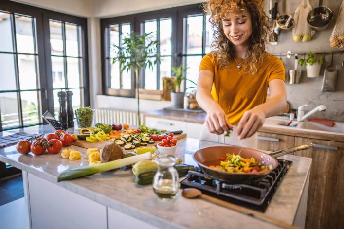 Femme préparant des légumes dans sa cuisine, concentrée sur la préparation d'un délicieux repas