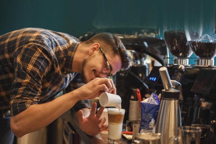 Junge Barista, die die perfekte Menge Milch in einen Latte Macchiato