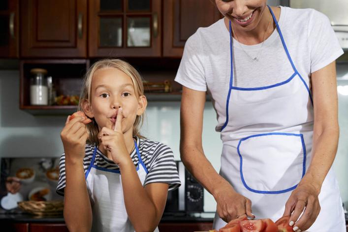 Mädchen, das mit ihrer Mama kocht und dabei ein Stillezeichen macht