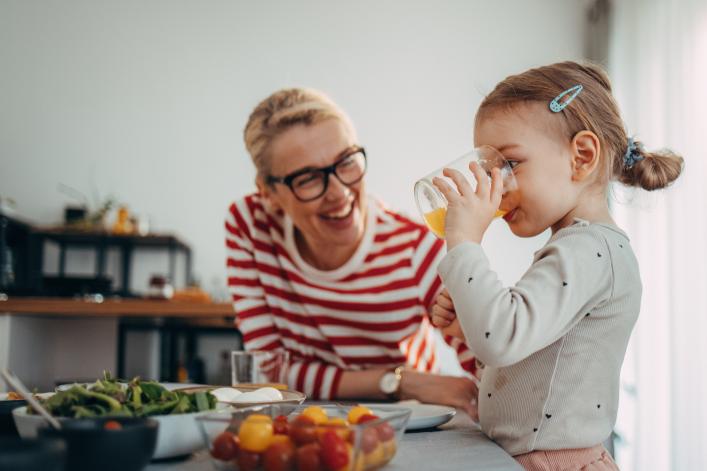 Fille mignonne debout dans la cuisine, buvant un verre de jus d’orange 