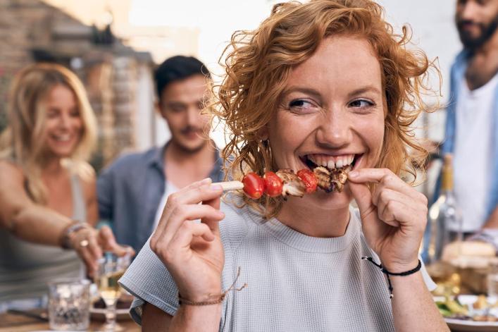 Person mit Tomatenspieß bei einem Essen im Freien mit Freunden.