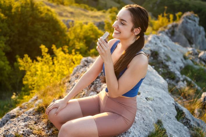 Person sitzt auf Felsen und isst Snack.