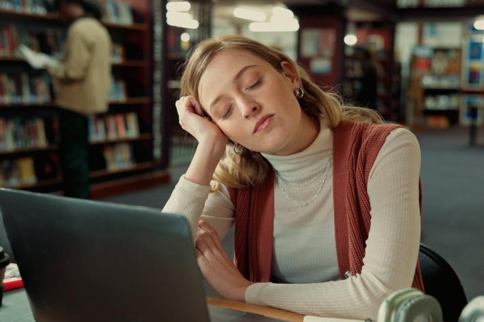 Student schläft in der Bibliothek mit einem Laptop.