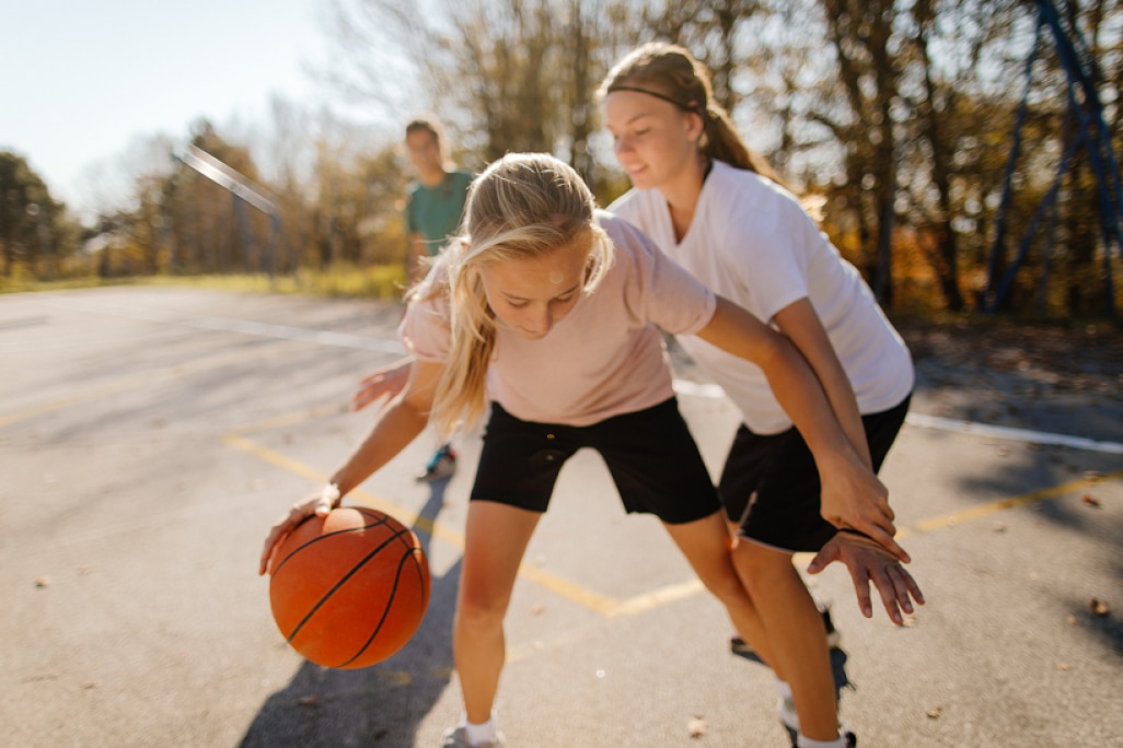 Deux personnes jouent au basket-ball en plein air sur un terrain ensoleillé.
