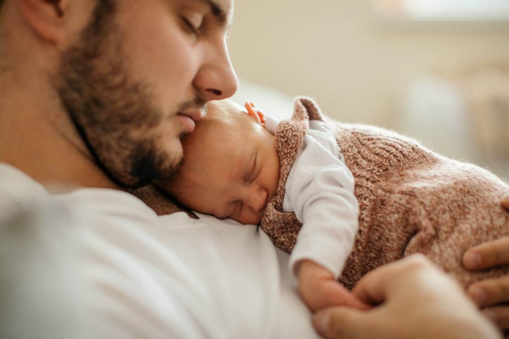 Ein Neugeborenes schläft friedlich in den Armen seines Vaters