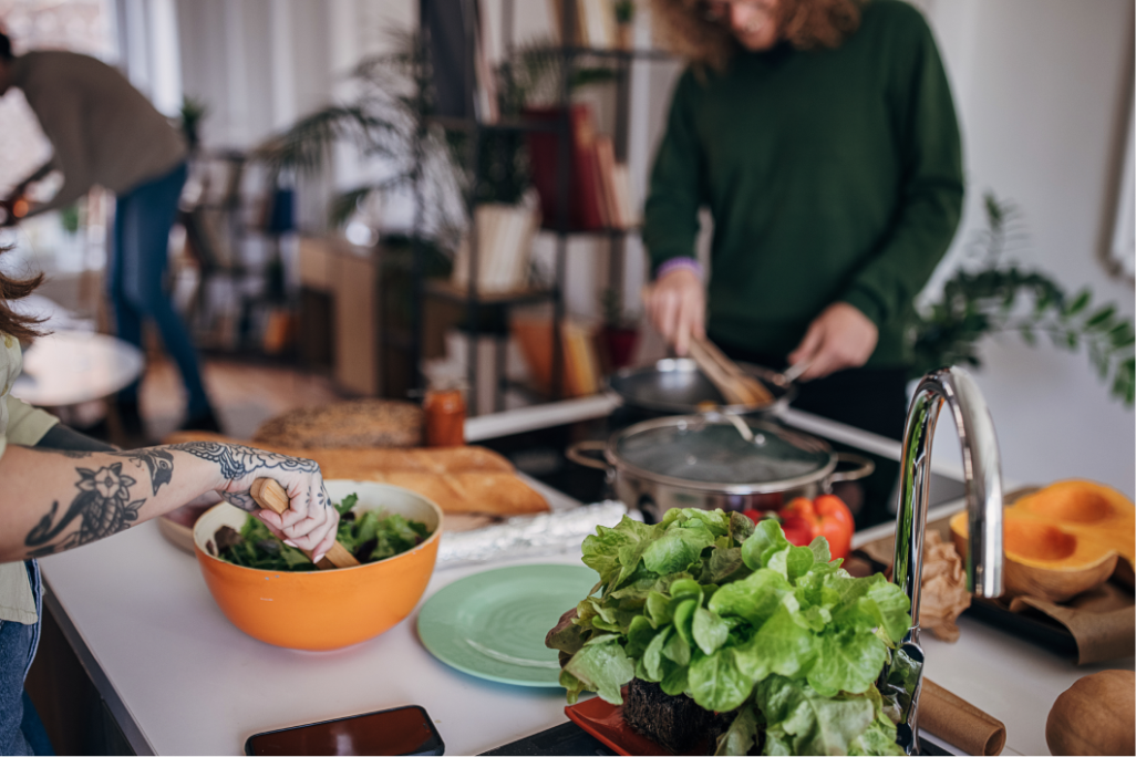 Freunde bereiten gemeinsam einen Salat mit frischem Blattgemüse in der Küche zu 