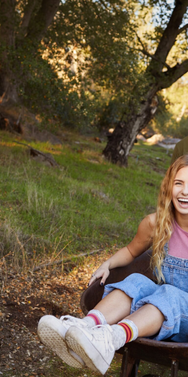 Lachende-frau-wird-von-ihrem-freund-in-einer-schubkarre-geschoben