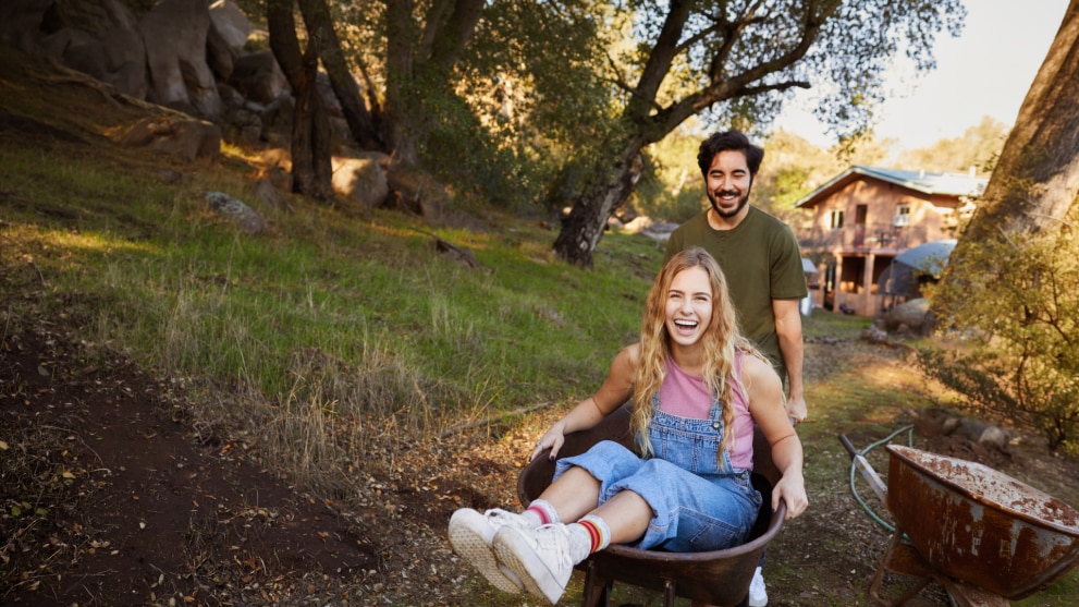 Lachende-frau-wird-von-ihrem-freund-in-einer-schubkarre-geschoben