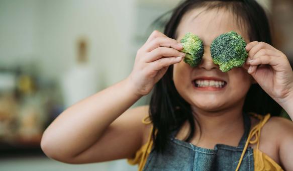 Mädchen hat Spassin der Küche und hält sich Brokkoli vor die Augen