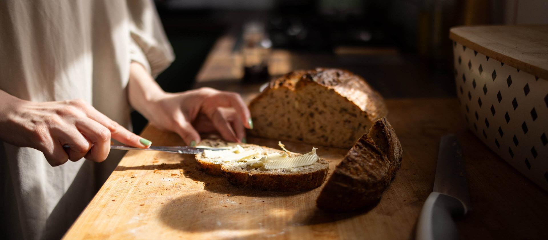Frau streicht Butter auf Vollkornbrot in der Küche