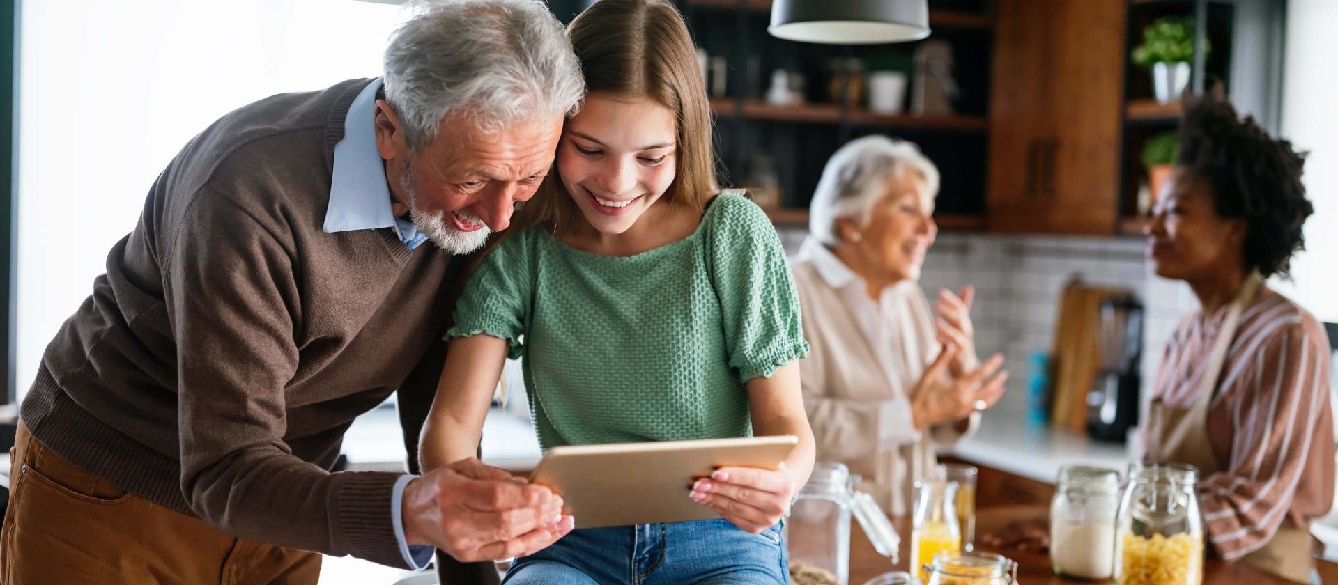 Grossvater und seine Enkelin in der Küche, die Informationen auf ihrem Tablet ansehen