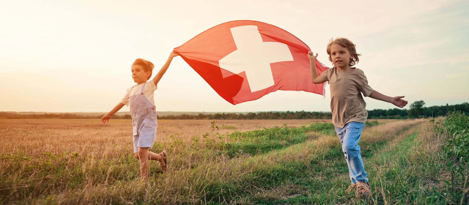 Zwei Jungen rennen und tragen eine Schweizer Fahne zum 1. August