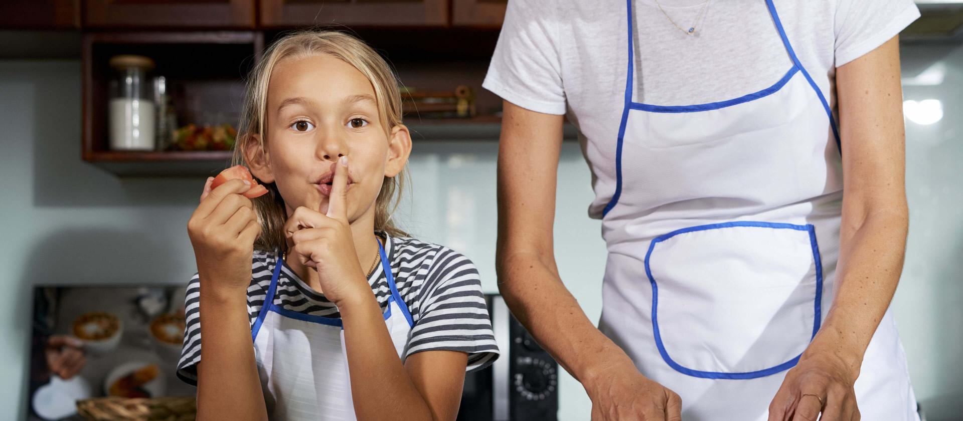 Fillette cuisinant avec sa maman, tandis qu'elle fait un signe de silence