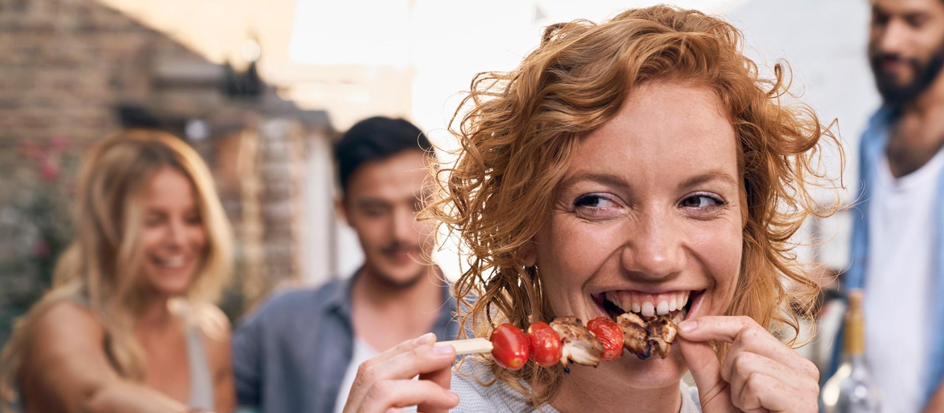 Person mit Tomatenspieß bei einem Essen im Freien mit Freunden.