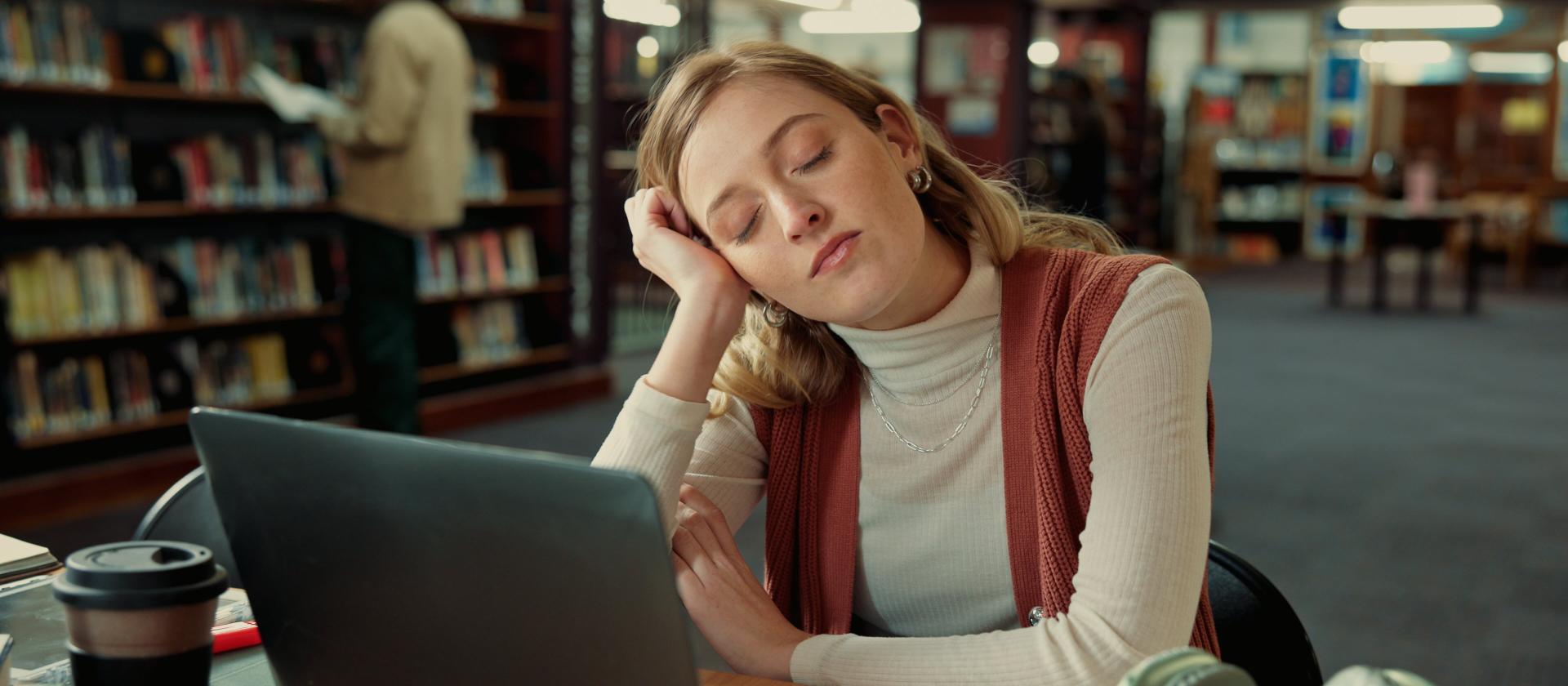 Student schläft in der Bibliothek mit einem Laptop.