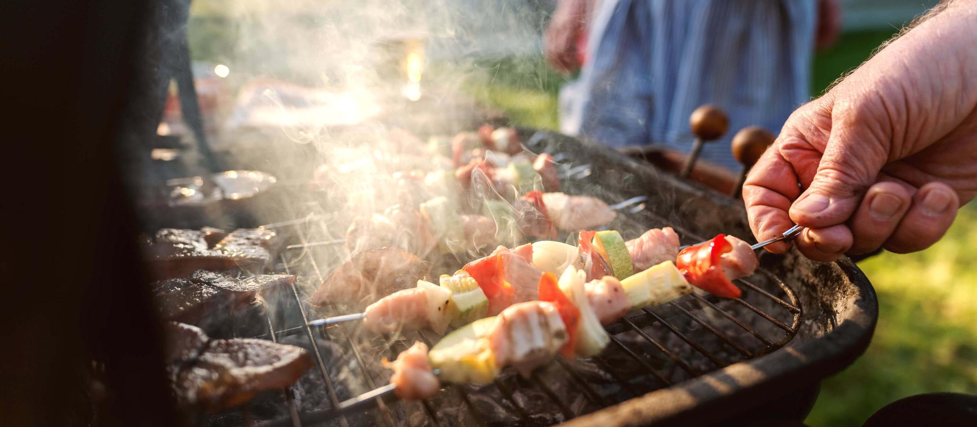 Gros plan sur un grand‑père attentionné surveillant les grillades de viande et de légumes pour régaler toute la famille