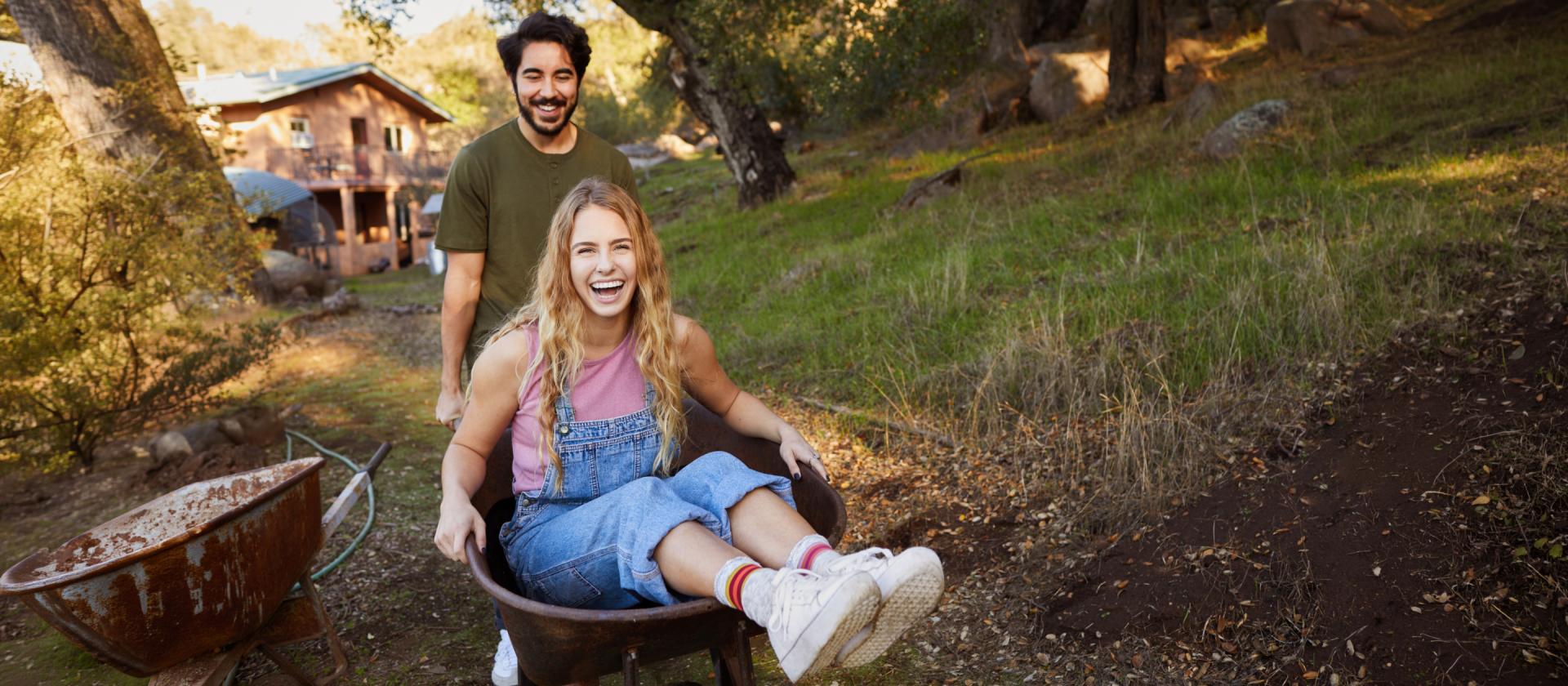 Lachende-frau-wird-von-ihrem-freund-in-einer-schubkarre-geschoben