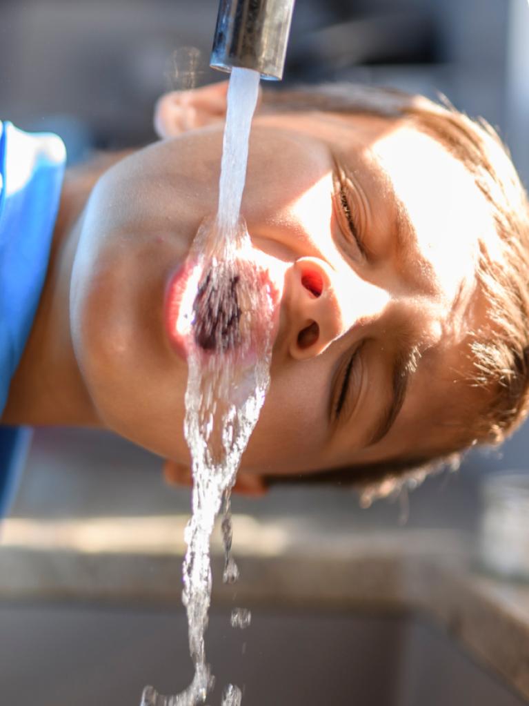 Un garçon boit au robinet 