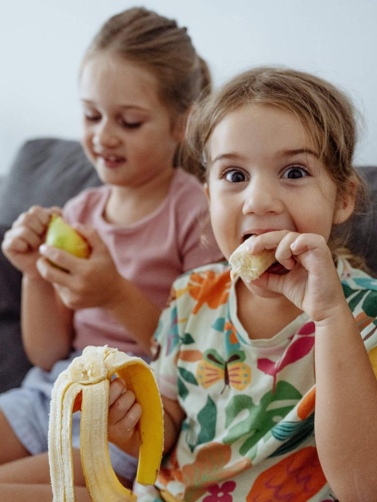 Jeunes filles partageant des fruits, l’une souriante avec une banane.