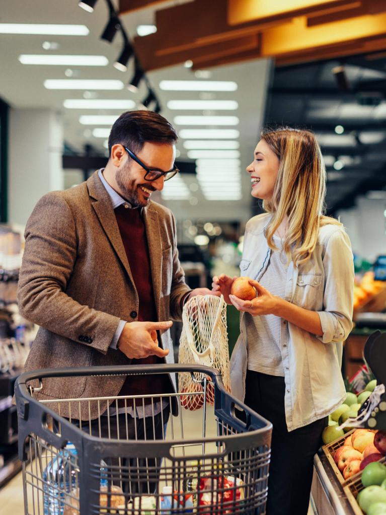 Couple heureux choisissant des oranges dans un sac en filet réutilisable à l’épicerie