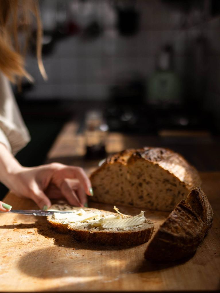 Frau streicht Butter auf Vollkornbrot in der Küche