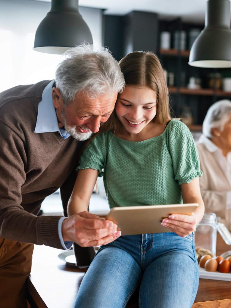 Grossvater und seine Enkelin in der Küche, die Informationen auf ihrem Tablet ansehen