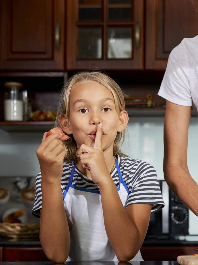 Mädchen, das mit ihrer Mama kocht und dabei ein Stillezeichen macht