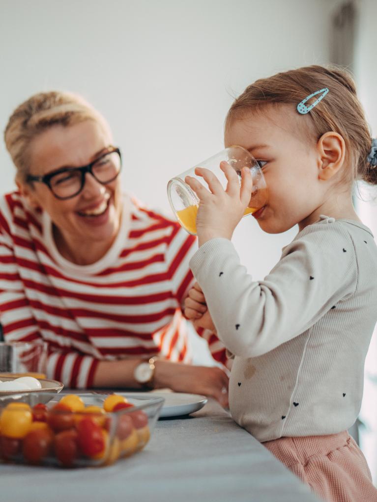 Fille mignonne debout dans la cuisine, buvant un verre de jus d’orange 