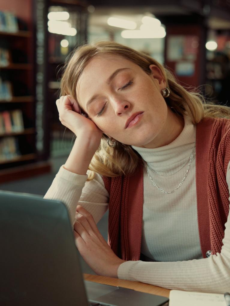 Student schläft in der Bibliothek mit einem Laptop.