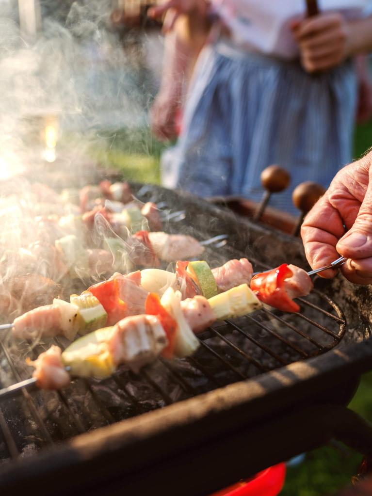 Gros plan sur un grand‑père attentionné surveillant les grillades de viande et de légumes pour régaler toute la famille