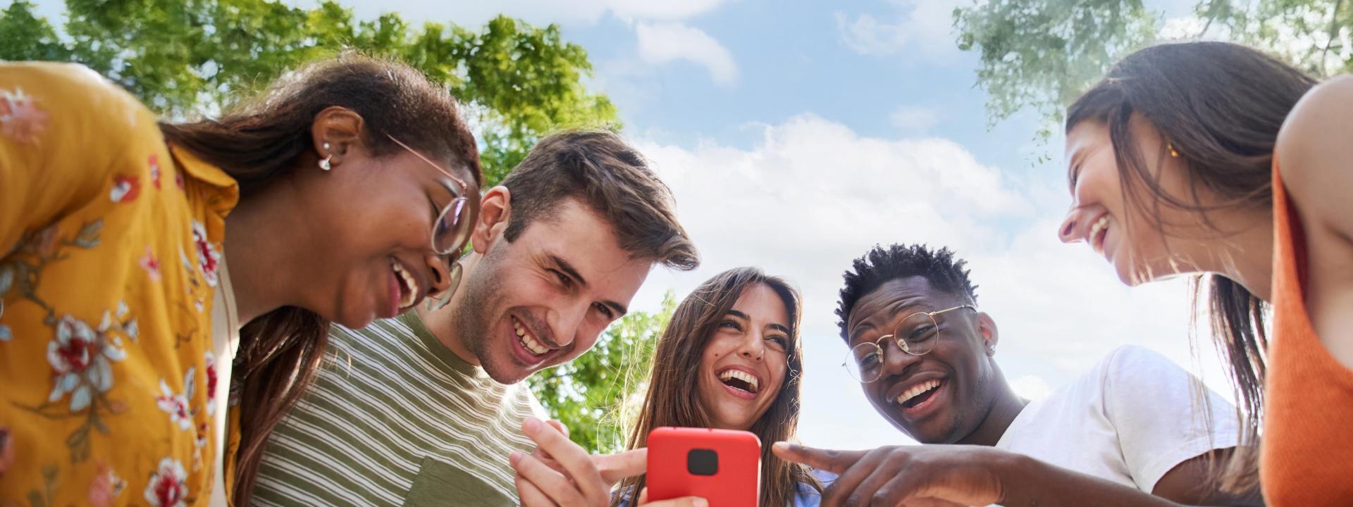 Lachende junge Leute zeigen auf den Bildschirm eines Smartphones.