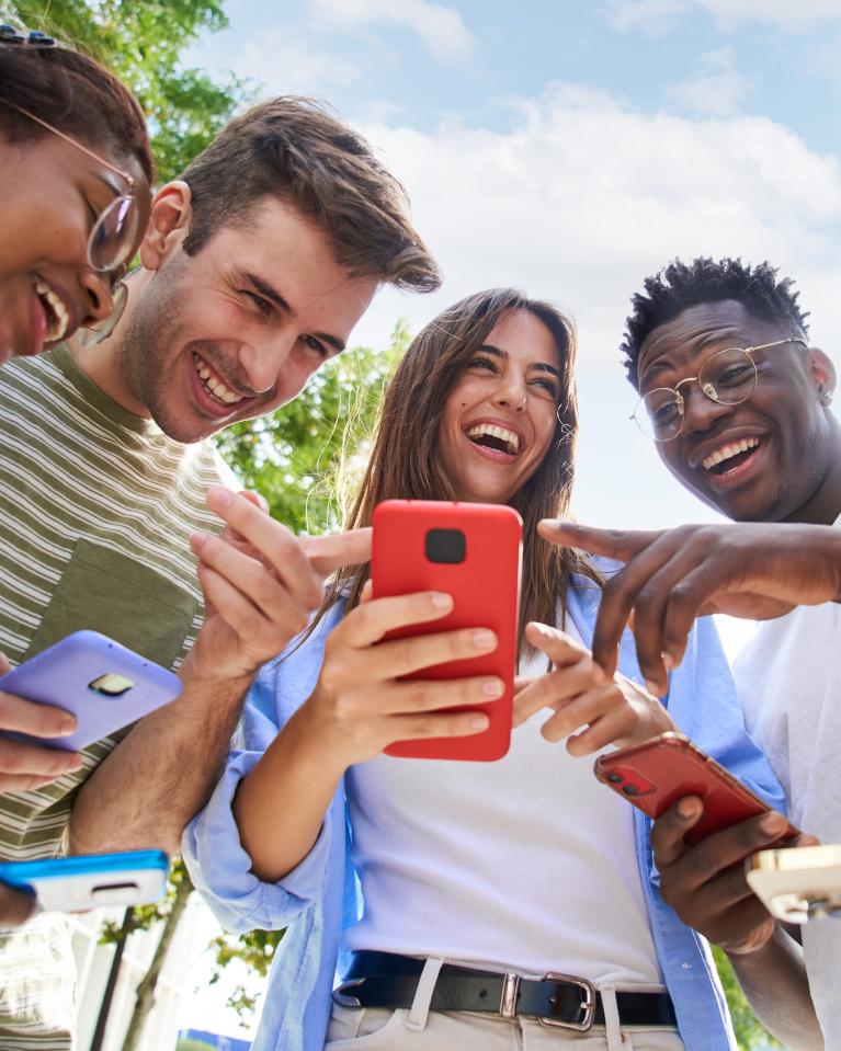 Lachende junge Leute zeigen auf den Bildschirm eines Smartphones.