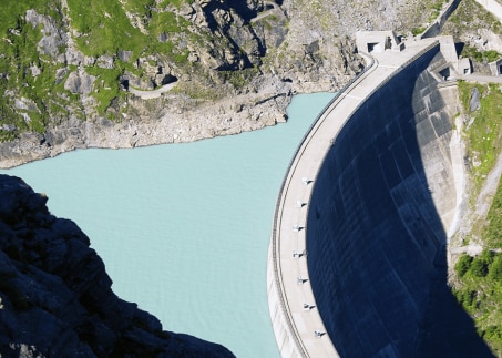 Luftaufnahme eines großen Staudamms mit türkisfarbenem Wasser und Felsen.