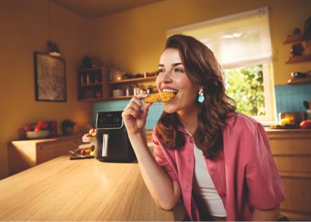 Junge Frau geniesst knusprigen Snack aus dem Airfryer