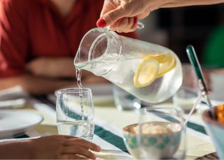 Frau schenkt ein Glas Wasser mit Zitrone ein