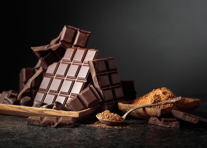 Un bol rempli de tablettes de chocolat noir et une cuillère de poudre de cacao.