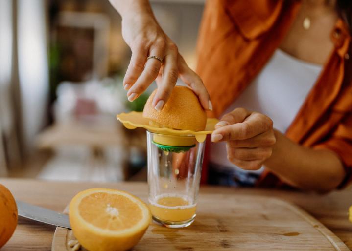 Junge Frau, die beim Frühstück Orangen auspresst.